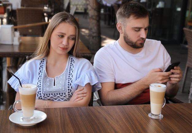 Junger Mann mit Smartphone ignoriert seine Freundin im Café im Freien Langweiliges Date