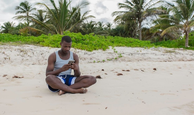 Junger Mann mit Smartphone sitzt auf dem Strandsand