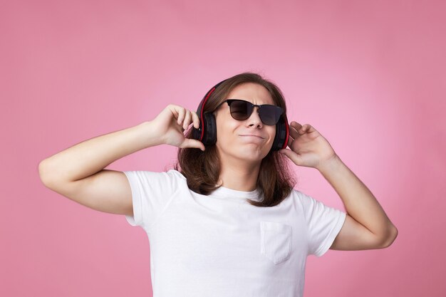 Junger mann mit sonnenbrille hört musik mit kopfhörern und tanzt auf rosa hintergrund