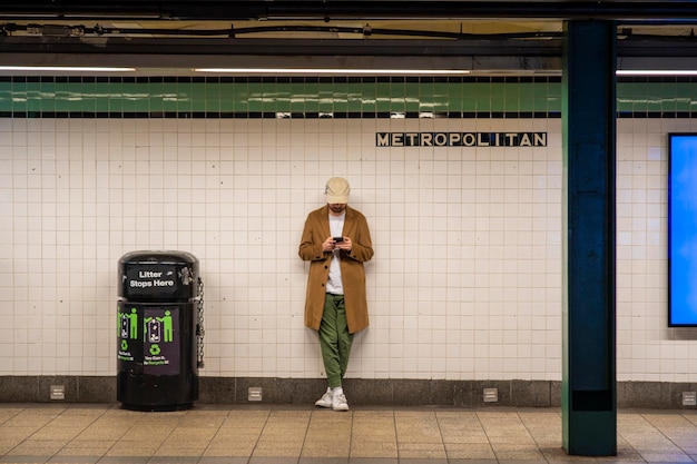 Junger Mann mit Streetstyle-Mantel, Hut, an der Station der New Yorker U-Bahnlinie ohne Menschen