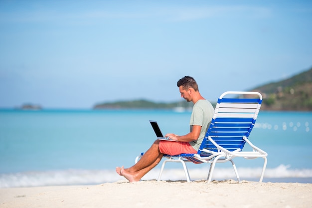 Junger Mann mit Tablet-Computer während der tropischen Strandferien