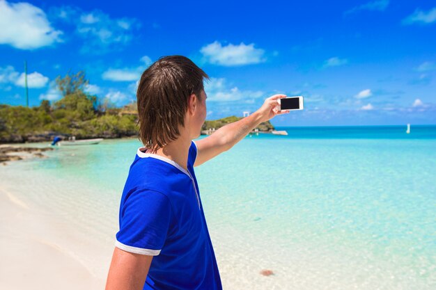 Junger Mann mit Telefon am tropischen karibischen Strand