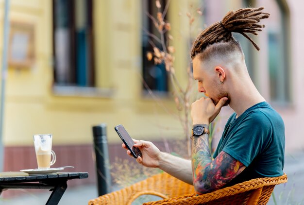 Junger Mann mit Telefon sitzt am Tisch in einem Café in der Stadt