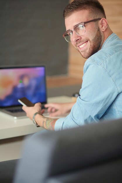 Junger Mann mit Telefon und arbeitet am Laptop.