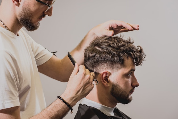 Junger Mann mit trendigem Haarschnitt am Friseurladen. Barber macht die Frisur und Bart schneiden.