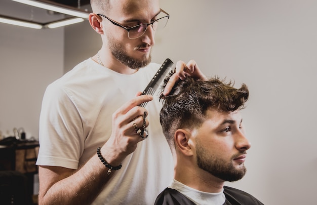 Junger Mann mit trendigem Haarschnitt am Friseurladen. Barber macht die Frisur und Bart schneiden.