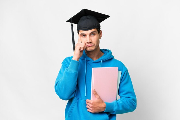 Junger Mann mit Universitätsabschluss über isoliertem weißem Hintergrund, der eine Idee denkt