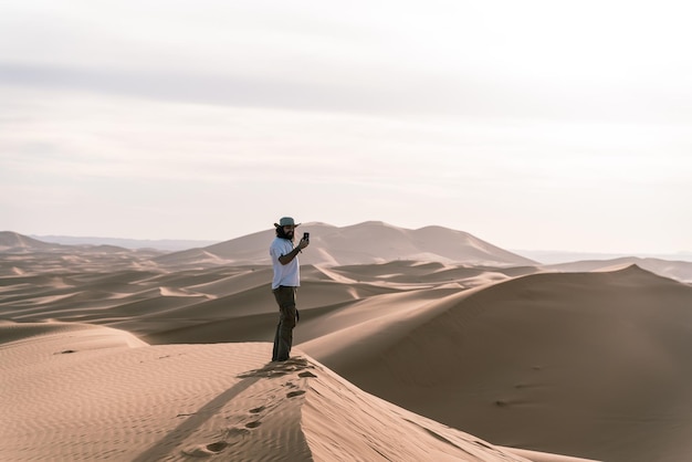 Foto junger mann mitten in der wüste macht ein foto mit seinem handy