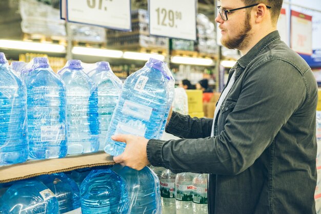 Junger Mann nimmt Wasser aus dem Regal des Ladens