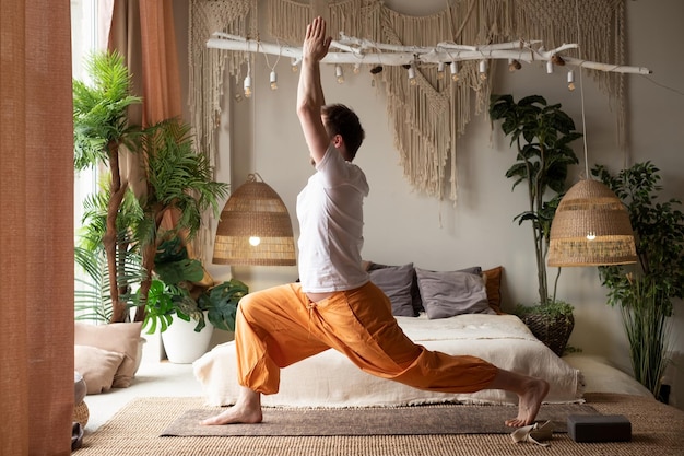Junger Mann praktiziert Yoga in Kriegerpose oder Virabhadrasana zu Hause