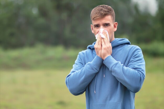 Junger Mann putzt Nase im Taschentuch