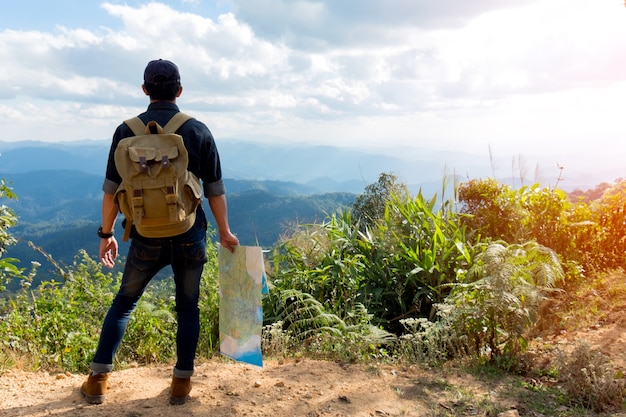 Junger Mann-Reisender mit Kartenrucksackentspannung im Freien mit felsigen Bergen auf Hintergrund Sommerferien und Lebensstil, die Konzept wandern