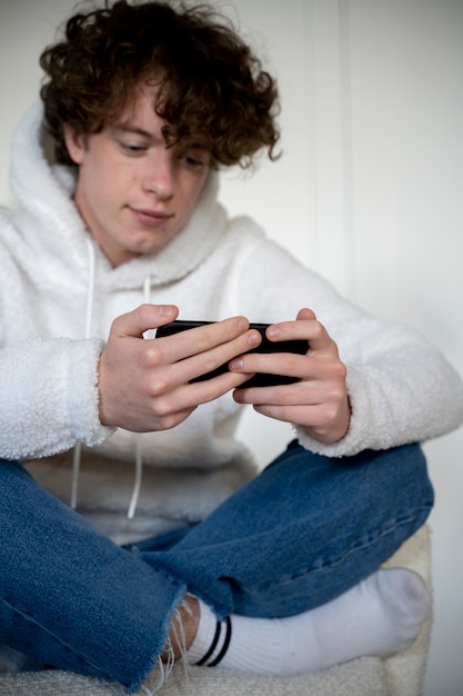 Foto junger mann schaut sich mit seinem smartphone einen film an, während er auf einem stuhl sitzt