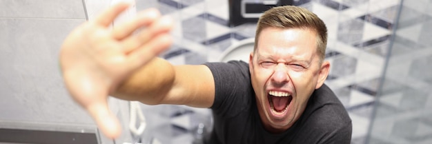 Foto junger mann schreit, während er auf toilettendarmproblemen und verstopfungskonzept sitzt