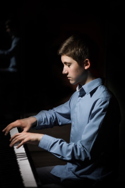 Junger Mann sitzt am Klavier, Junge spielt emotional das Tasteninstrument in der Musikschule, Schüler lernt, Hände zu spielen, Pianist, schwarzer dunkler Hintergrund, vertikal