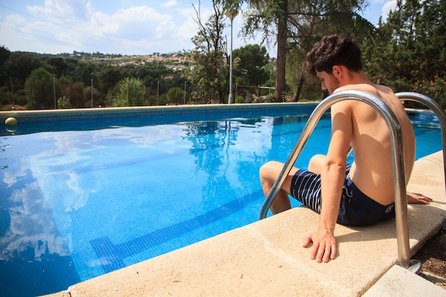 Junger Mann sitzt am Rand des Pools