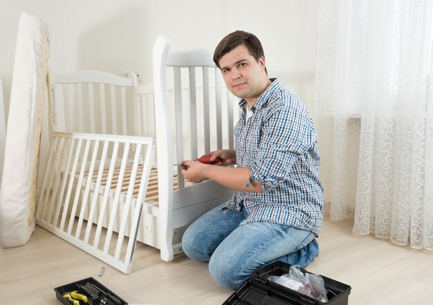 Junger Mann sitzt auf dem Boden und repariert das Kinderbett