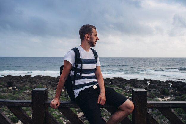 Junger Mann sitzt auf einem Geländer am Meer