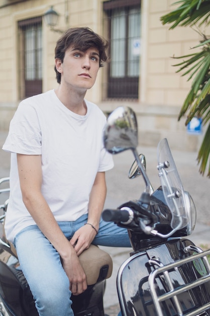 Foto junger mann sitzt auf einem roller. in jeans und weißem hemd gekleidet.