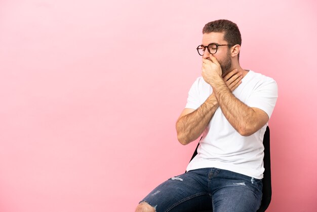 Junger Mann sitzt auf einem Stuhl über isoliertem rosa Hintergrund und hustet viel