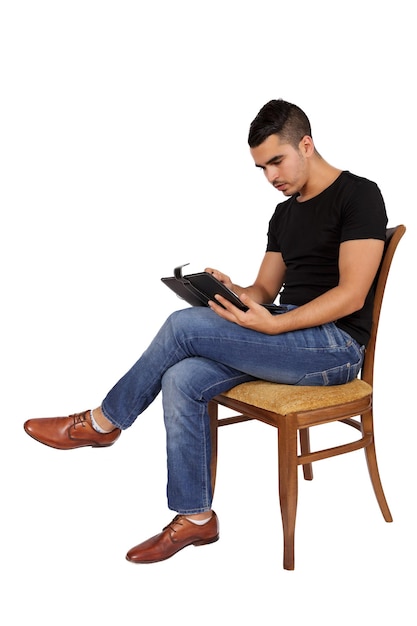Junger Mann sitzt auf einem Stuhl und schaut auf ein Tablet auf weißem Hintergrund