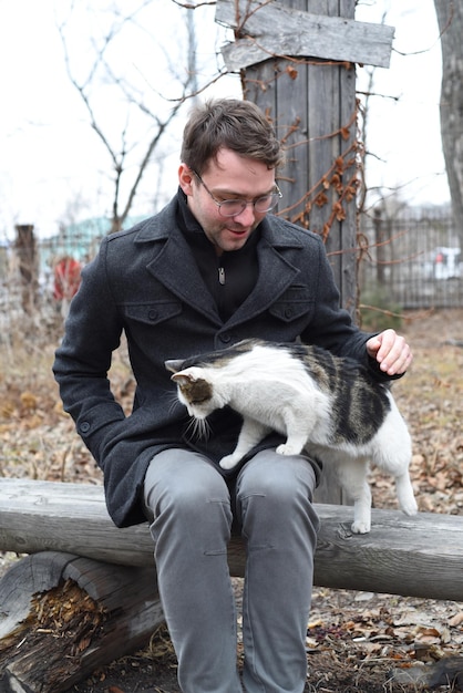 Junger Mann sitzt auf einer Bank und streichelt eine Katze