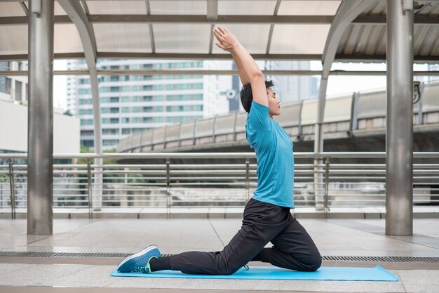 Junger Mann sitzt Übung mit Pose Yoga Meditation auf blauer Matte in der Stadt in