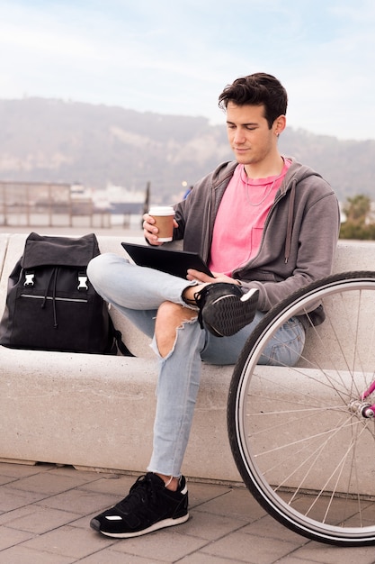 Junger Mann sitzt draußen mit Tablet