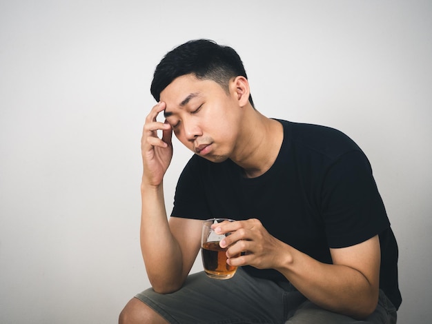 Junger Mann sitzt fühlt sich angestrengt, Alkohol in der Hand zu halten, weißer Hintergrund