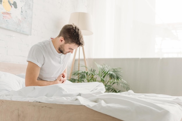 Foto junger mann sitzt im bett und leidet unter bauchschmerzen