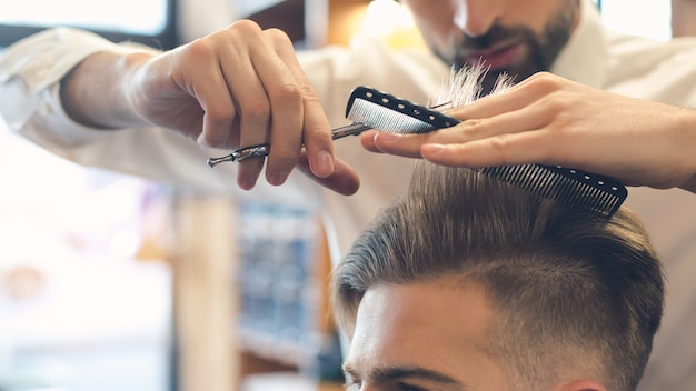 Junger Mann sitzt in einem Friseursalon, während der Friseur die Haare schneidet