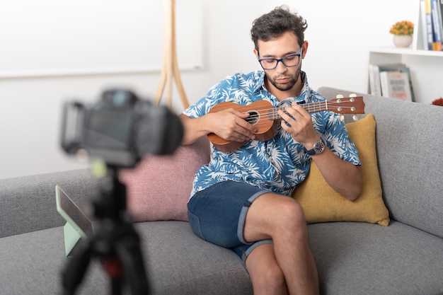 Junger Mann sitzt in einem Wohnzimmer und nimmt ein Video auf, das Musik mit einer Ukulele spielt