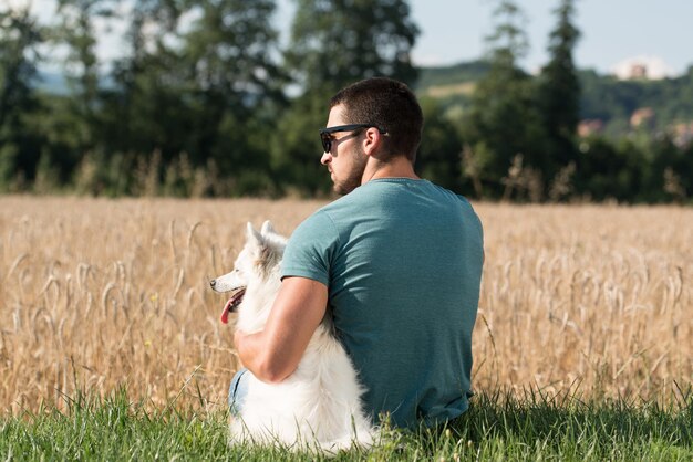 Junger Mann sitzt mit Hund Deutscher Spitz im abgeernteten Feld