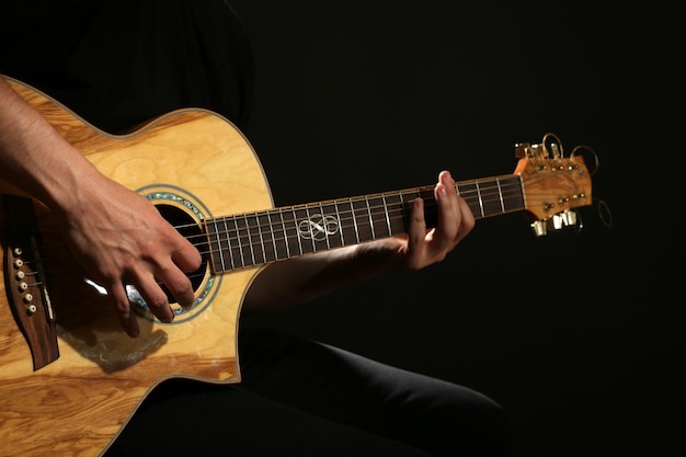 Junger Mann spielt auf Akustikgitarre auf dunklem Hintergrund