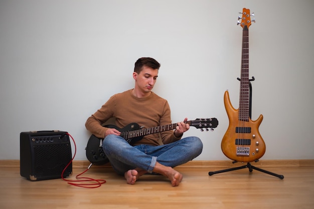 Junger Mann spielt auf einer Gitarre mit Wand im Hintergrund