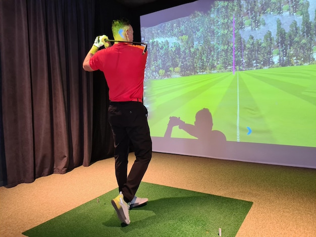 Junger Mann spielt drinnen Golf Golfsimulator