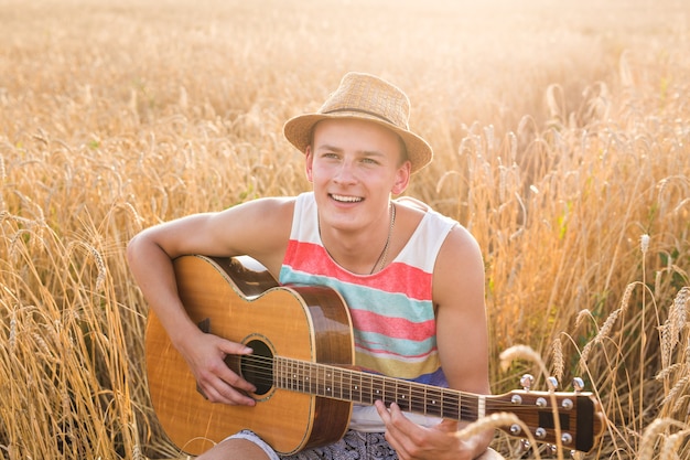 Junger Mann spielt Gitarre auf dem Gebiet bei Sonnenuntergang.