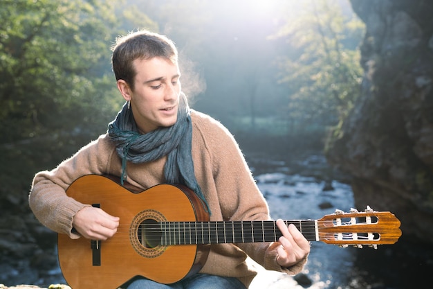 Junger Mann spielt Gitarre neben einem Fluss