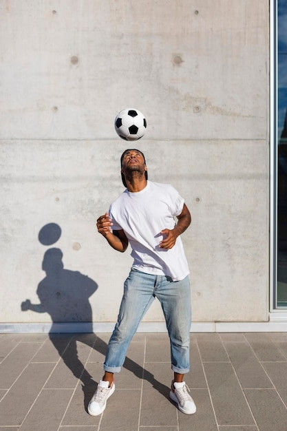 Junger Mann spielt mit Fußball vor Betonwand