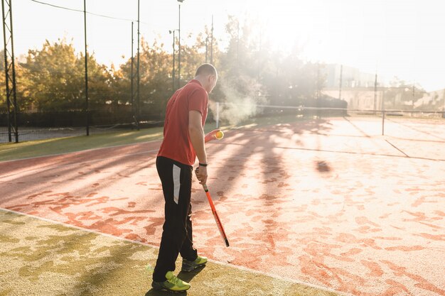 Junger Mann spielt Tennis am frischen sonnigen Morgen