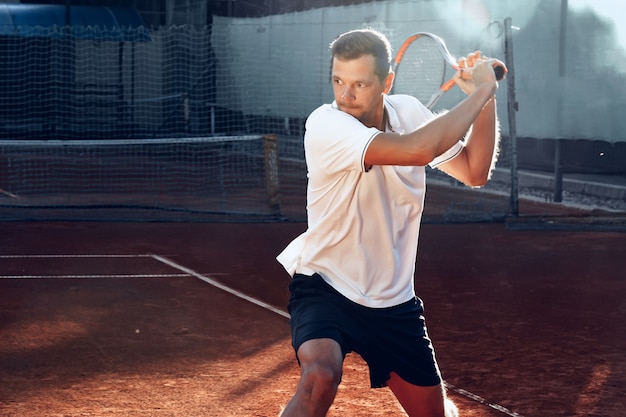 Foto junger mann spielt tennis draußen auf tennisplatz am morgen