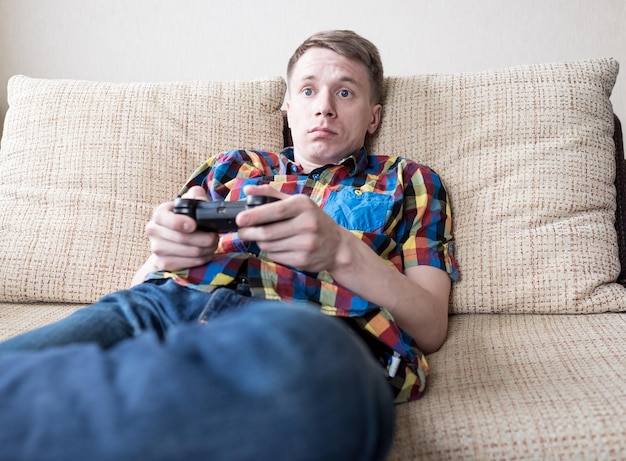 Junger Mann spielt Videospiele, sitzt auf dem Sofa und hält die Fernbedienung in der Hand