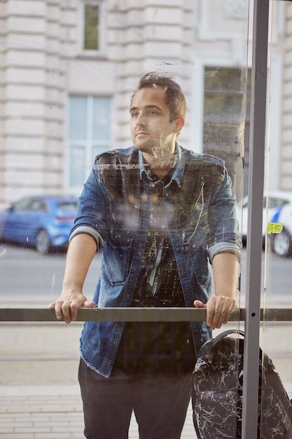 Junger Mann steht hinter Fenster der öffentlichen Verkehrsstation.