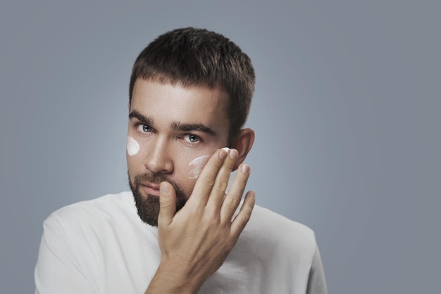 Junger Mann trägt Feuchtigkeitscreme auf sein Gesicht auf