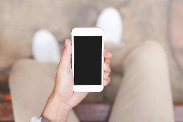 Junger Mann trägt kariertes Hemd. Schließen Sie die Hand mit dem Handy während der Ruhe auf dem Sofa. Sitzen in der Nachricht auf dem Handy Smartphone während der Pause entspannen.