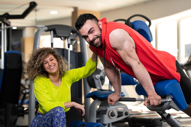 Junger Mann trainiert im Fitnessstudio und macht mit Hilfe ihres Trainers Rückenübungen an der Maschine