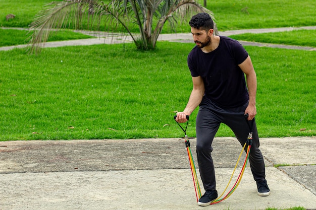 junger Mann trainiert mit elastischen Bändern und macht Armübungen im Freien in einem Park