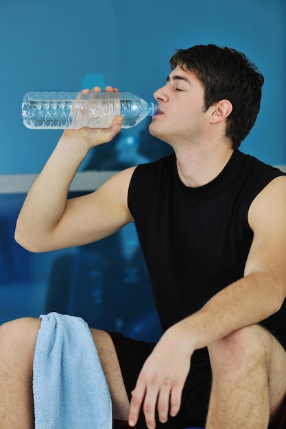 Junger Mann trinkt Wasser beim Fitnesstraining im Sportverein