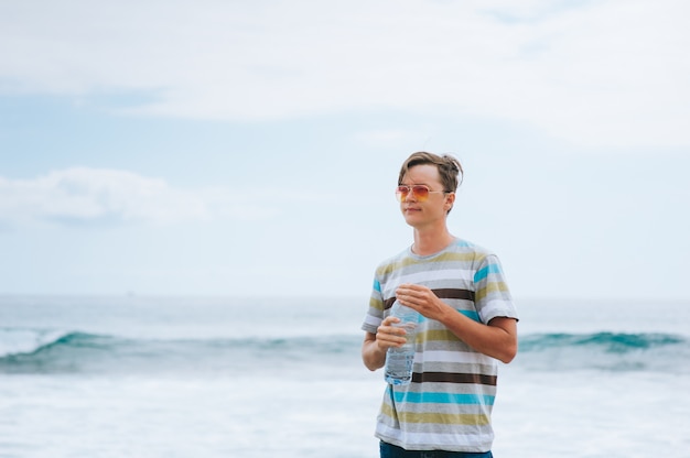 junger Mann Trinkwasser am Strand