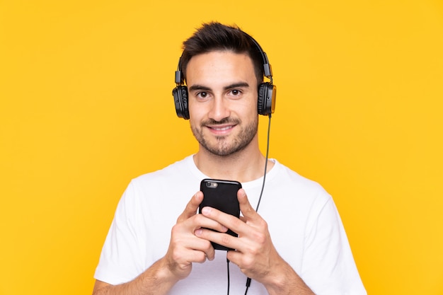 Junger Mann über gelbe hörende Musik mit einem Handy und schauender Front